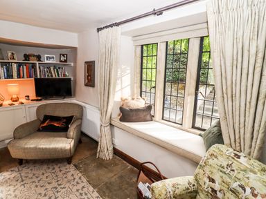 A sitting area with an armchair, window seat with cushions, bookshelves, and a TV at The Small House Near Bourton-On-The-Water