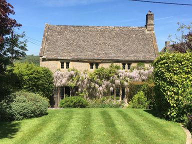 A stone house with a tiled roof surrounded by plants and a green lawn at The Small House Near Bourton-On-The-Water