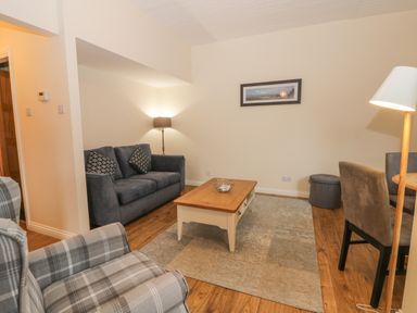 A living room with a grey sofa, plaid armchair, wooden coffee table, floor lamps, and dining chairs at Bugle in Saltburn-By-The-Sea