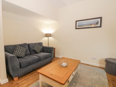 A sitting room with a gray sofa and patterned cushions a wooden coffee table a floor lamp a framed picture on the wall and a gray ottoman at Bugle in Saltburn-By-The-Sea