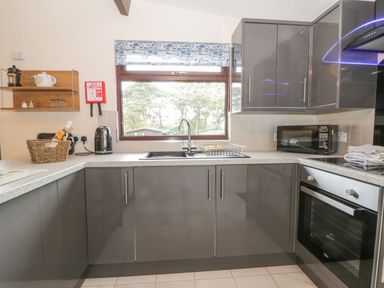 A kitchen with grey cabinets a window above the sink a microwave and an oven at Bugle in Saltburn-By-The-Sea