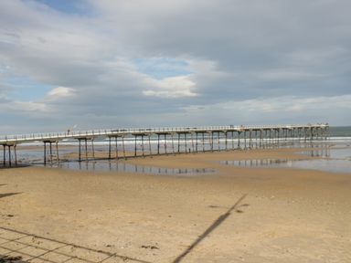 A beach with a long pier extending over the sand and water at Bugle in Saltburn-By-The-Sea
