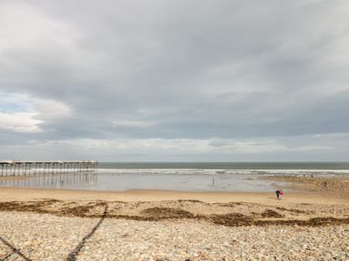A beach with pebbles and sand a pier extending into the sea and people walking at Lavender Lodge in Saltburn-By-The-Sea