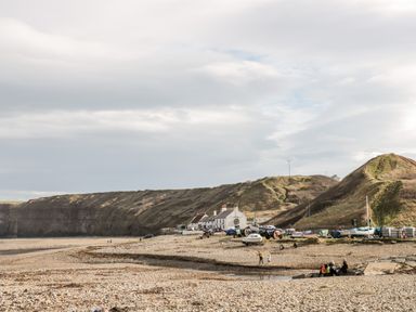 A pebble beach with boats, cars, houses, and hills at Lavender Lodge in Saltburn-By-The-Sea
