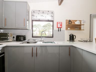 A kitchen with grey cabinets a sink microwave toaster kettle and shelves with kitchen items at Lavender Lodge in Saltburn-By-The-Sea