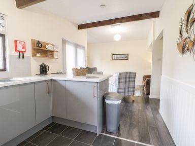 A kitchen with grey cabinets and a silver trash can next to a living room with armchairs and a sofa at Lavender Lodge in Saltburn-By-The-Sea
