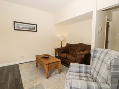 A living room with a brown sofa a plaid armchair a wooden coffee table and a framed picture on the wall at Lavender Lodge in Saltburn-By-The-Sea