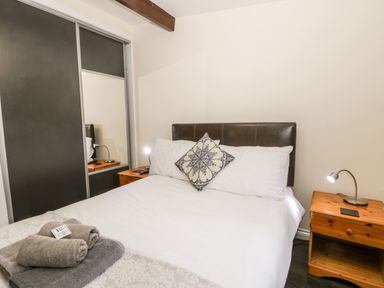 A bedroom with a double bed with white bedding and patterned pillow two wooden nightstands with lamps and a wardrobe with sliding doors at Lavender Lodge in Saltburn-By-The-Sea