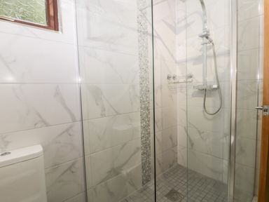 A shower area with a glass door a showerhead and tiled walls at Lavender Lodge in Saltburn-By-The-Sea