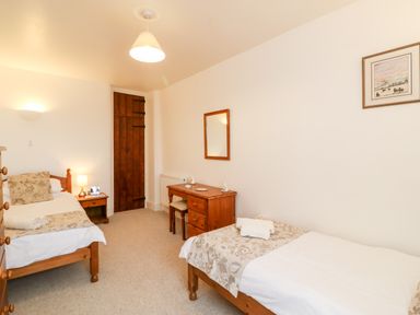 A bedroom with two single beds a wooden door and a wooden dressing table with a chair at Littleham Court Cottage in Littleham near Bideford