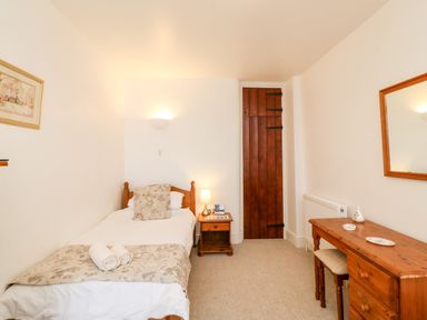 A small bedroom with a single bed wooden door wooden bedside table and wooden dresser with mirror at Littleham Court Cottage in Littleham near Bideford