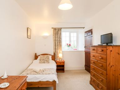 A bedroom with a single bed a wooden dresser a bedside table and a window with curtains at Littleham Court Cottage in Littleham near Bideford