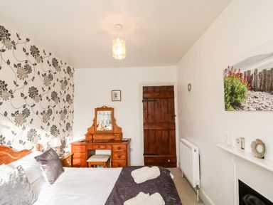 A bedroom with a bed and pillows a wooden dressing table with a mirror a wooden door and a radiator on the wall at Littleham Court Cottage Littleham near Bideford