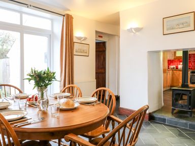 A dining room with a wooden table set with plates glasses and food a wood stove and kitchen with red tiles visible in the background at Littleham Court Cottage Littleham near Bideford
