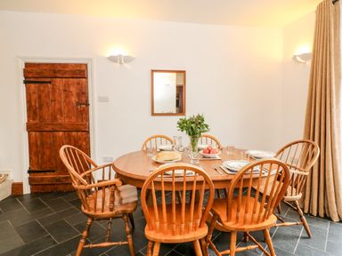 A dining room with a wooden table set with plates glasses and a flower vase around wooden chairs at Littleham Court Cottage in Littleham near Bideford