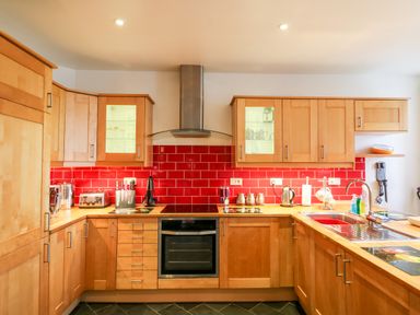 A kitchen with wooden cabinets red tiled backsplash and stainless steel appliances at Littleham Court Cottage in Littleham near Bideford