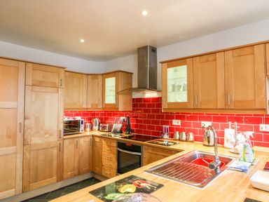 A kitchen with wooden cabinets red tiled backsplash stainless steel sink and appliances at Littleham Court Cottage Littleham near Bideford