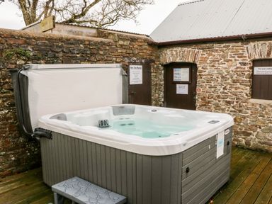 An outdoor hot tub surrounded by stone walls and wooden doors at Littleham Court Cottage in Littleham near Bideford