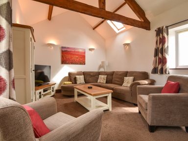 A living room with brown sofas a wooden coffee table a television and curtains at Littleham Court Cottage in Littleham near Bideford