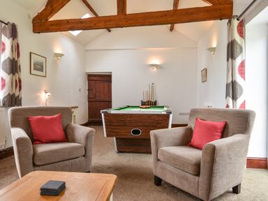 A sitting area with two armchairs red cushions and a pool table at Littleham Court Cottage in Littleham near Bideford