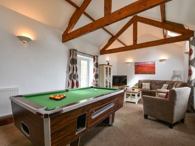 A living room with a pool table sofa a television and wooden beams at Littleham Court Cottage in Littleham near Bideford