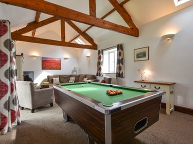 A games room with a pool table a sofa and armchair under wooden beams at Littleham Court Cottage in Littleham near Bideford