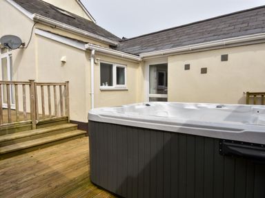 An outdoor wooden deck with stairs and a hot tub next to a beige house at Littleham Court Cottage in Littleham near Bideford
