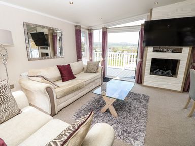 A living room with two sofas a glass coffee table a mounted television and fireplace and a door leading to a balcony at Crosswinds 67 in Bembridge