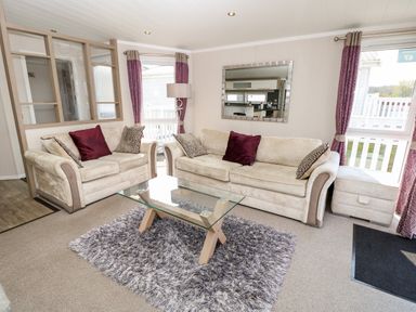 A living room with two beige sofas pillows a glass coffee table and purple curtains at Crosswinds 67 in Bembridge