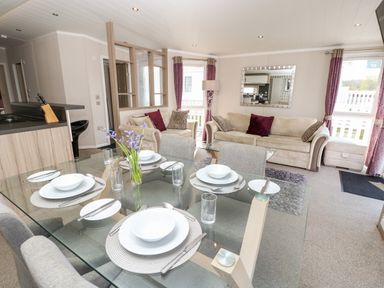 A dining table set for four with plates and cutlery in a living room with sofas and purple curtains at Crosswinds 67 in Bembridge