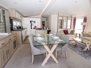 An open plan living room and kitchen with a glass dining table set with plates and bowls at Crosswinds 67 in Bembridge