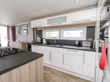 A kitchen with white cabinets black countertops a gas stove toaster kettle and wooden flooring at Crosswinds 67 in Bembridge