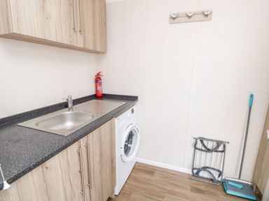 A utility room with a sink washing machine fire extinguisher mop and dustpan at Crosswinds 67 in Bembridge