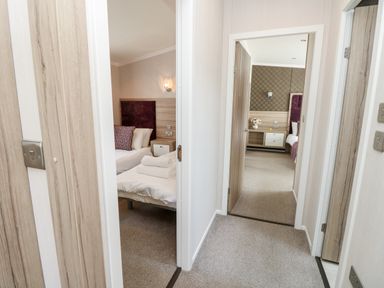 A hallway showing two bedrooms with beds pillows and bedside tables at Crosswinds 67 in Bembridge