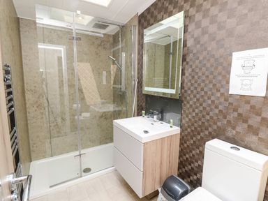 A bathroom with a shower enclosure a sink with cabinet a mirror a toilet and a trash bin at Crosswinds 67 in Bembridge