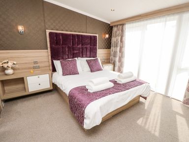A bedroom with a double bed with purple cushions and headboard and towels on the bed at Crosswinds 67 in Bembridge