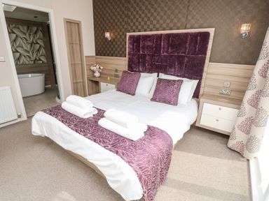 A bedroom with a double bed headboard bedside tables with lamps and an open door to a bathroom at Crosswinds 67 in Bembridge