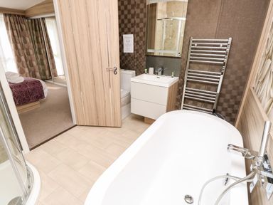 A bathroom with a bathtub a sink a toilet a shower and a towel rack visible through an open door to a bedroom with a bed at Crosswinds 67 in Bembridge