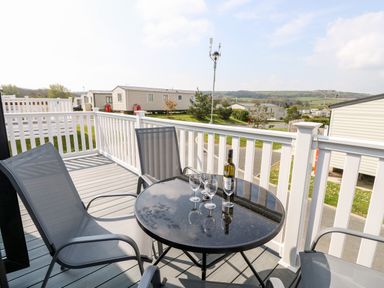 An outdoor deck with a round glass table with a bottle and wine glasses and four chairs at Crosswinds 67 in Bembridge