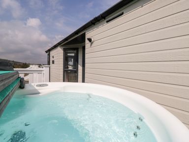 An outdoor hot tub on a deck next to a beige house with horizontal siding at Crosswinds 67 in Bembridge
