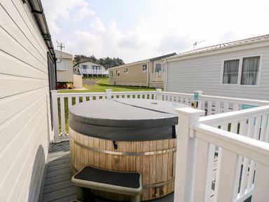 An outdoor deck area with a covered wooden hot tub surrounded by white railings at Crosswinds 67 in Bembridge