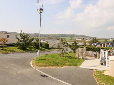 An outdoor area with mobile homes trees a paved road and hills in the background at Crosswinds 67 in Bembridge