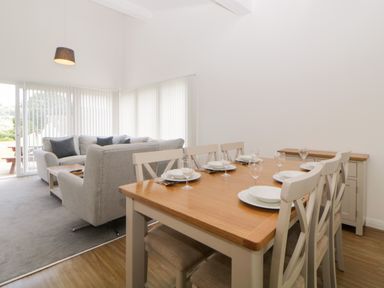 A dining area with a wooden table set for six and a living area with sofas near large windows at Harcombe House Bungalow 3 in Chudleigh