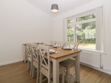 A dining room with a wooden table and six chairs set with plates glasses and cutlery next to a window at Harcombe House Bungalow 3 in Chudleigh