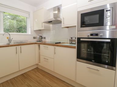 A kitchen with white cabinets wooden countertops a built-in oven microwave stove kettle toaster and a window showing greenery at Harcombe House Bungalow 3 in Chudleigh