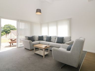 A living room with a gray sectional sofa, armchair, wooden coffee table, vertical blinds, and sliding glass door at Harcombe House Bungalow 4 in Chudleigh