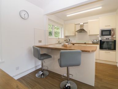 A kitchen with wooden countertops two stools a wall clock and built in oven at Harcombe House Bungalow 4 in Chudleigh