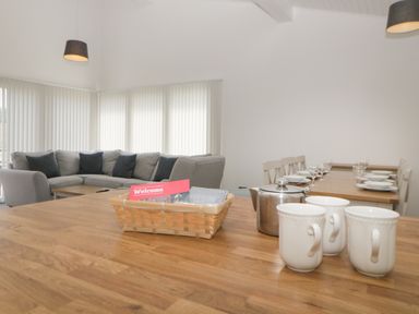 A seating area with a grey sofa and black cushions with a wooden dining table set with plates and glasses at Harcombe House Bungalow 4 in Chudleigh