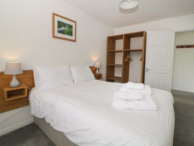 A bedroom with a double bed with white linens two bedside lamps an open wooden wardrobe and folded towels on the bed at Harcombe House Bungalow 4 Chudleigh