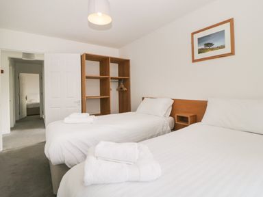 A bedroom with two single beds white linens wooden shelving and a framed picture on the wall at Harcombe House Bungalow 4 in Chudleigh